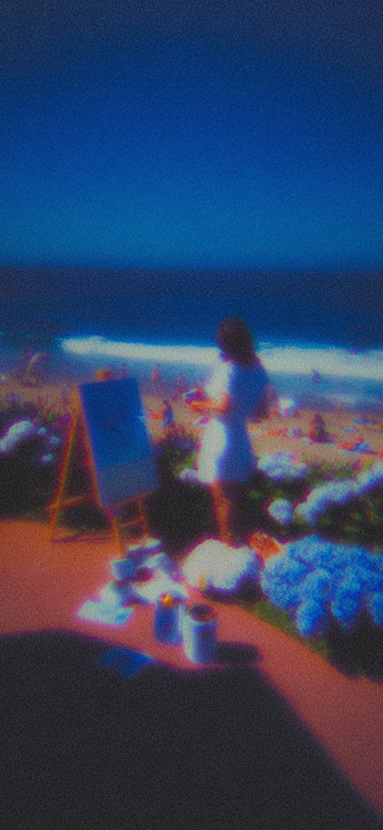 A person painting at an easel on a beach at dusk
