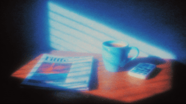 A coffee mug beside a folded newspaper on a sunlit desk.